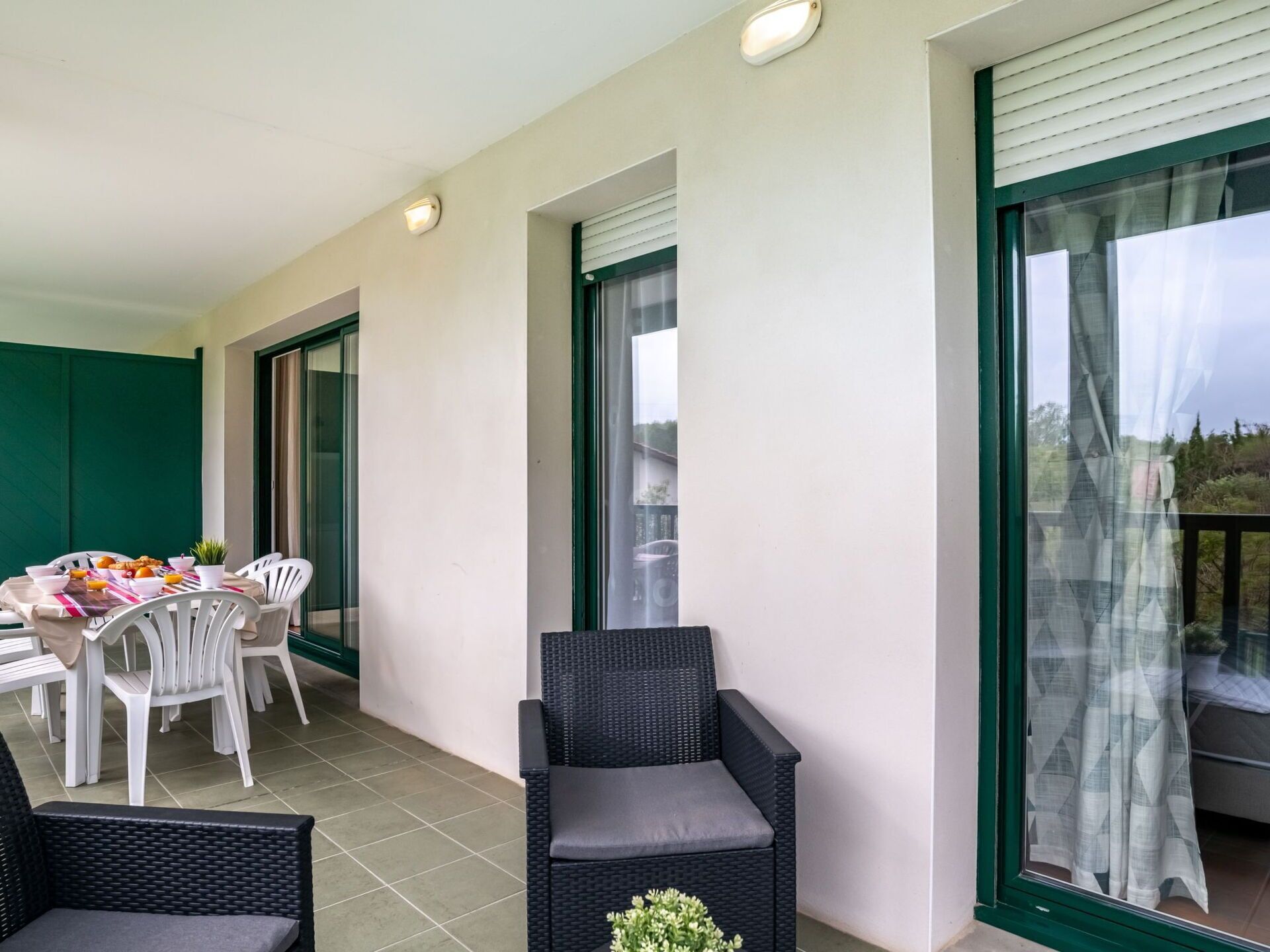 Een balkon met een eettafel voor twee personen, omringd door witte stoelen en een zwarte rieten stoel.