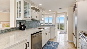A modern kitchen with white cabinetry, a built-in dishwasher, and a coffee maker. - Oceanfront | Turtle Dunes Luxury Penthouse | Intracoastal and Oceanfront Views | Double Balconies (Fernandina Beach)