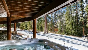 Ein Whirlpool unter einer Holnpergola mit verschneiter Landschaft und Tannen im Hintergrund.