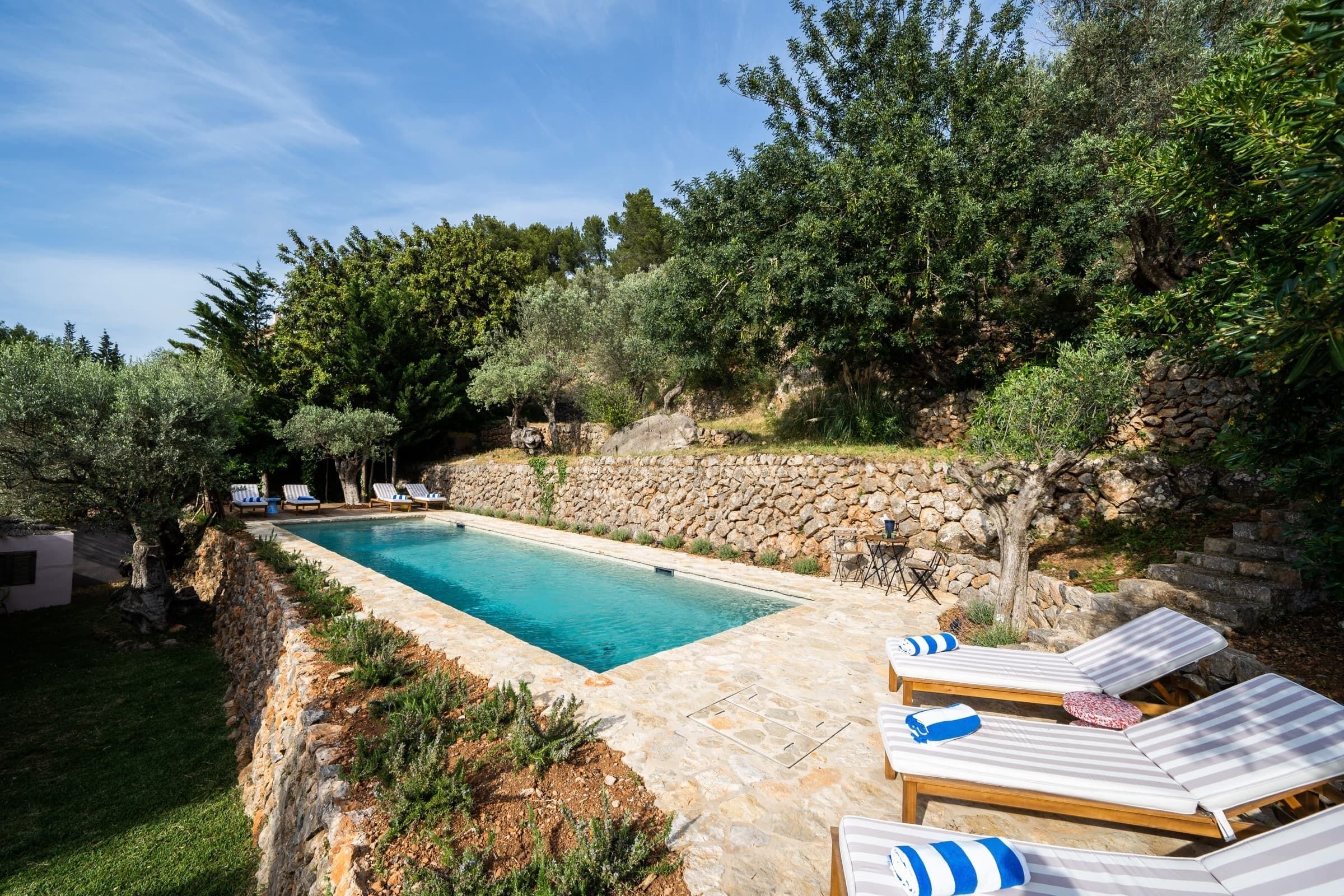 A rectangular swimming pool surrounded by stone walls, with lounge chairs and a stone wall on one side.