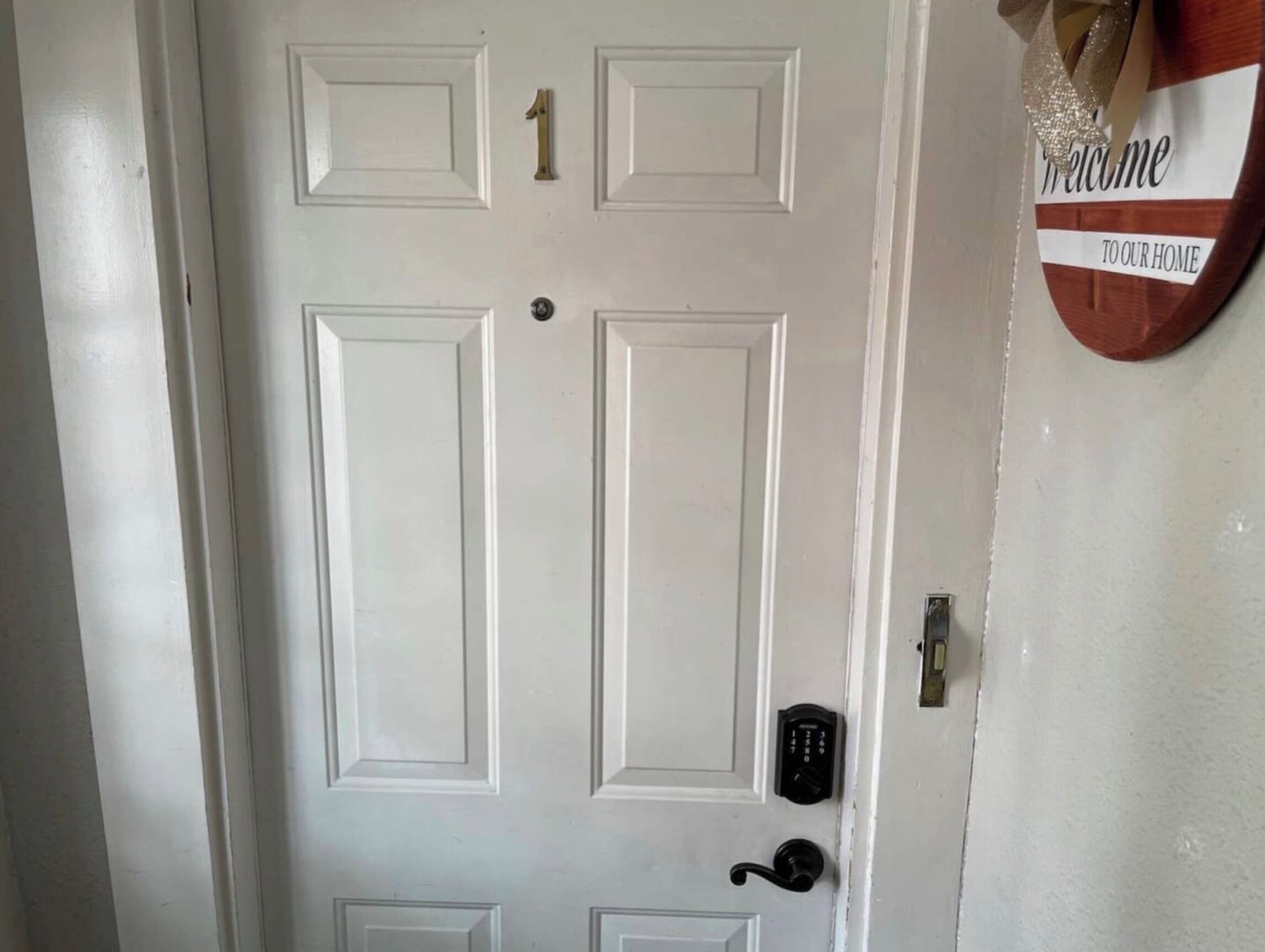 Una porta bianca con tastierino numerico, un cartello di benvenuto e un campanello.