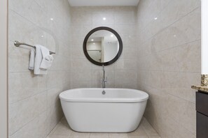 Een moderne badkamer met een vrijstaand bad, een ronde spiegel en een handdoekrek met handdoeken.