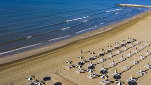 A beach with rows of sun loungers and umbrellas, a rocky breakwater, and calm ocean waves. - Lovely apartment for 4 people with WIFI, A/C, TV and patio (Ca' Savio)