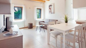 A modern living room with a wooden ceiling, white walls, a grey sofa, a dining table with chairs, and a TV on a stand. - Lovely apartment for 4 people with WIFI, A/C, TV and patio (Ca' Savio)