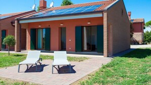 A modern house with a solar panel roof, a brick exterior, and a covered patio with two white lounge chairs. - Beautiful apartment for 6 guests with WIFI, TV and patio (Ca' Savio)