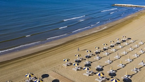 A beach with rows of sun loungers and umbrellas, a rocky breakwater, and calm ocean waves. - Beautiful apartment for 6 guests with WIFI, TV and patio (Ca' Savio)