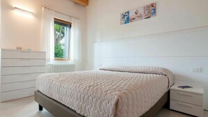 A bedroom with a bed, a nightstand, a dresser, a window with curtains, and a wall-mounted artwork. - Cosy apartment for 8 people with WIFI, A/C, TV and patio (Ca' Savio)