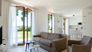 A modern living room with a sofa, armchair, and a small coffee table. There is a kitchen area with a dining table and chairs visible through an open door. - Beautiful apartment for 6 people with A/C, WIFI and TV (Ca' Savio)