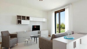 A modern living room with a sofa, armchair, TV, and a dining area with a table and chairs. - Beautiful apartment for 6 people with A/C, WIFI and TV (Ca' Savio)