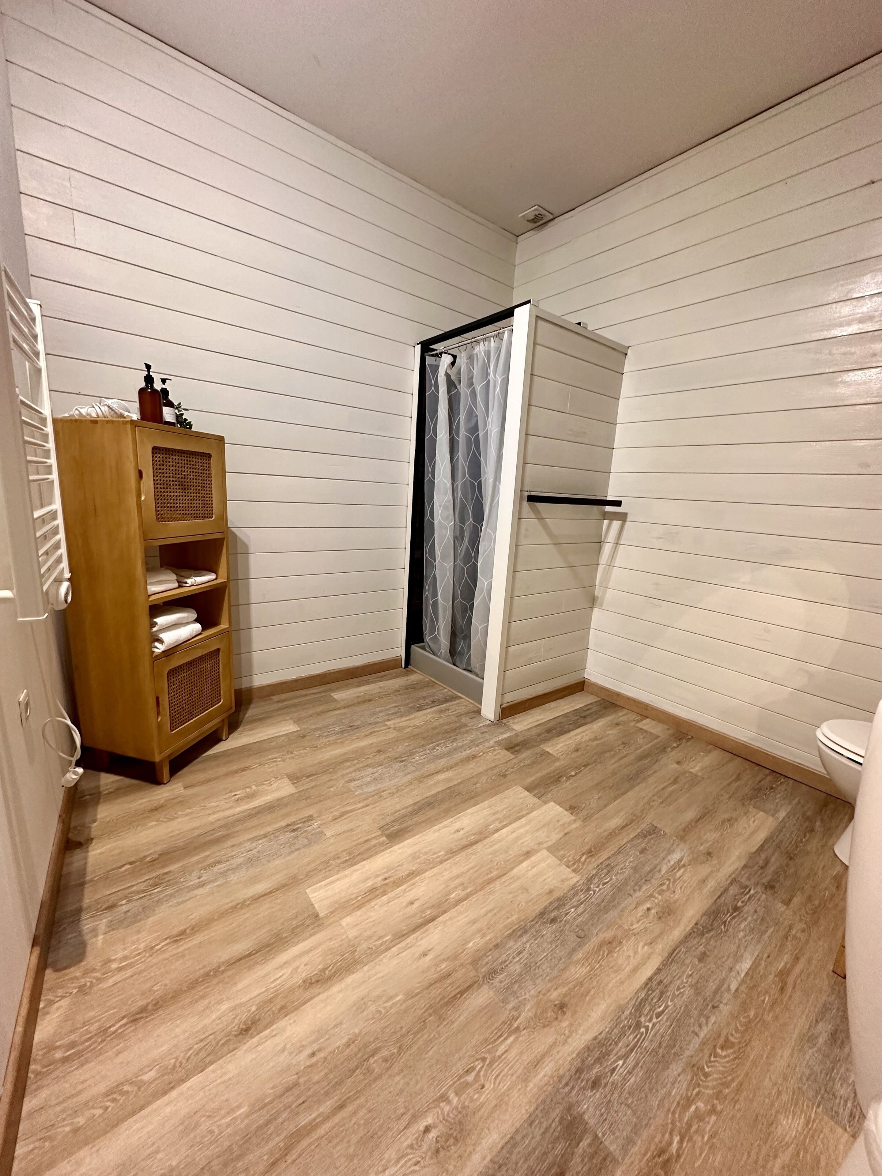 Une petite salle de bain avec un meuble en bois, un rideau de douche et des toilettes.