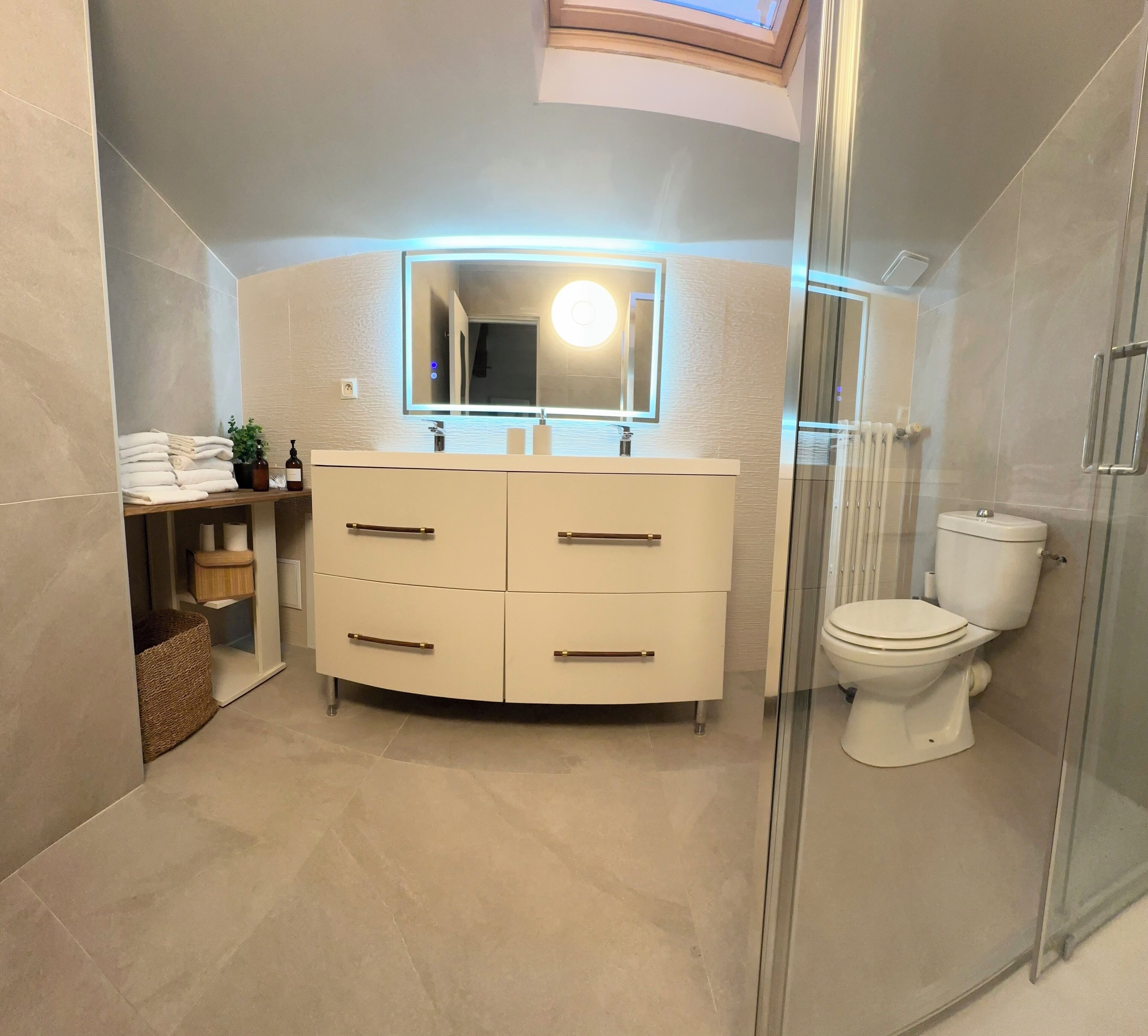 Een moderne badkamer met een douchecabine van glas, een wit toilet en een wastafel met spiegel en verlichting.