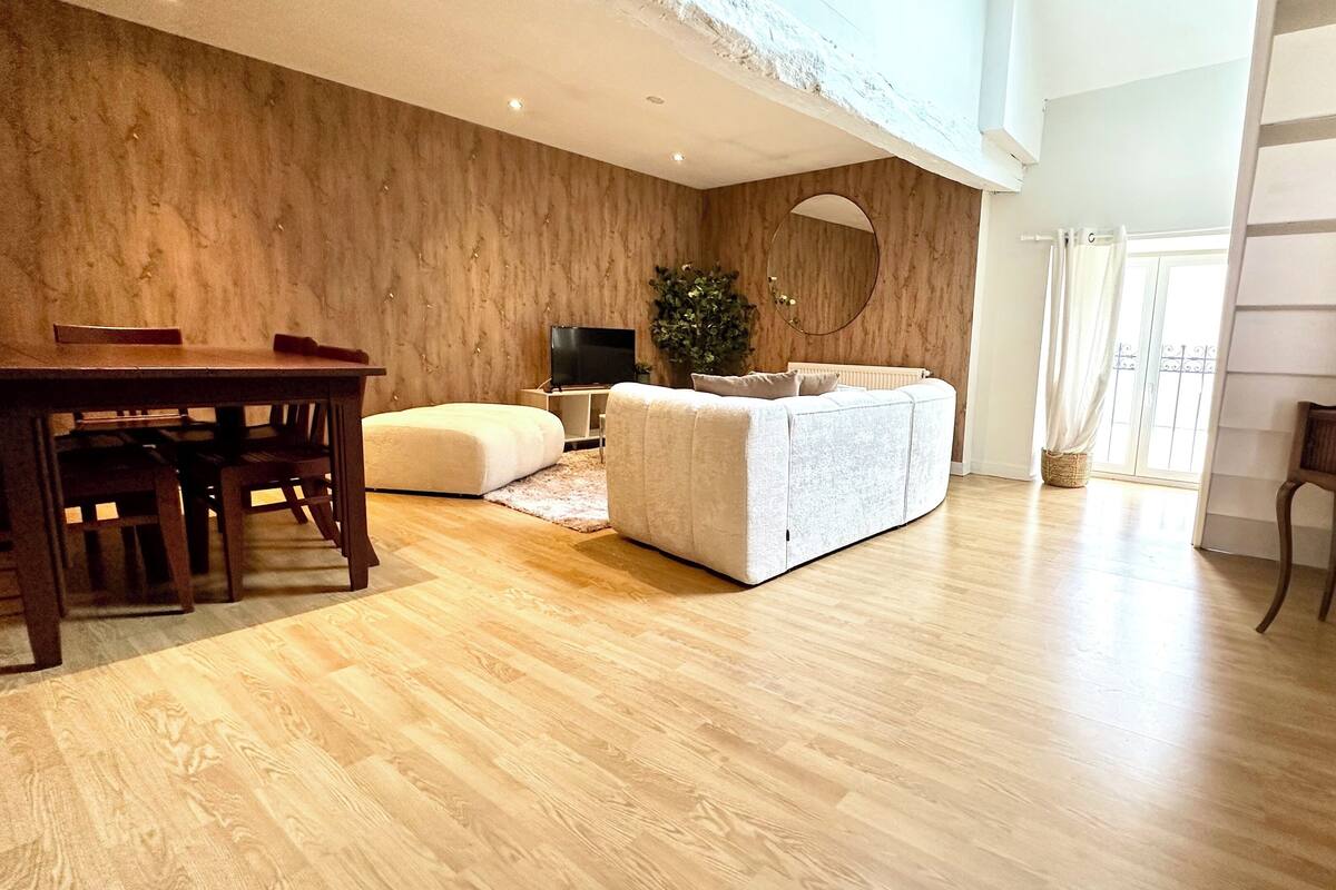 Ein geräumiges Wohnzimmer mit Holzboden, einer Couch, einem Fernseher und einem Essbereich mit Tisch und Stühlen.