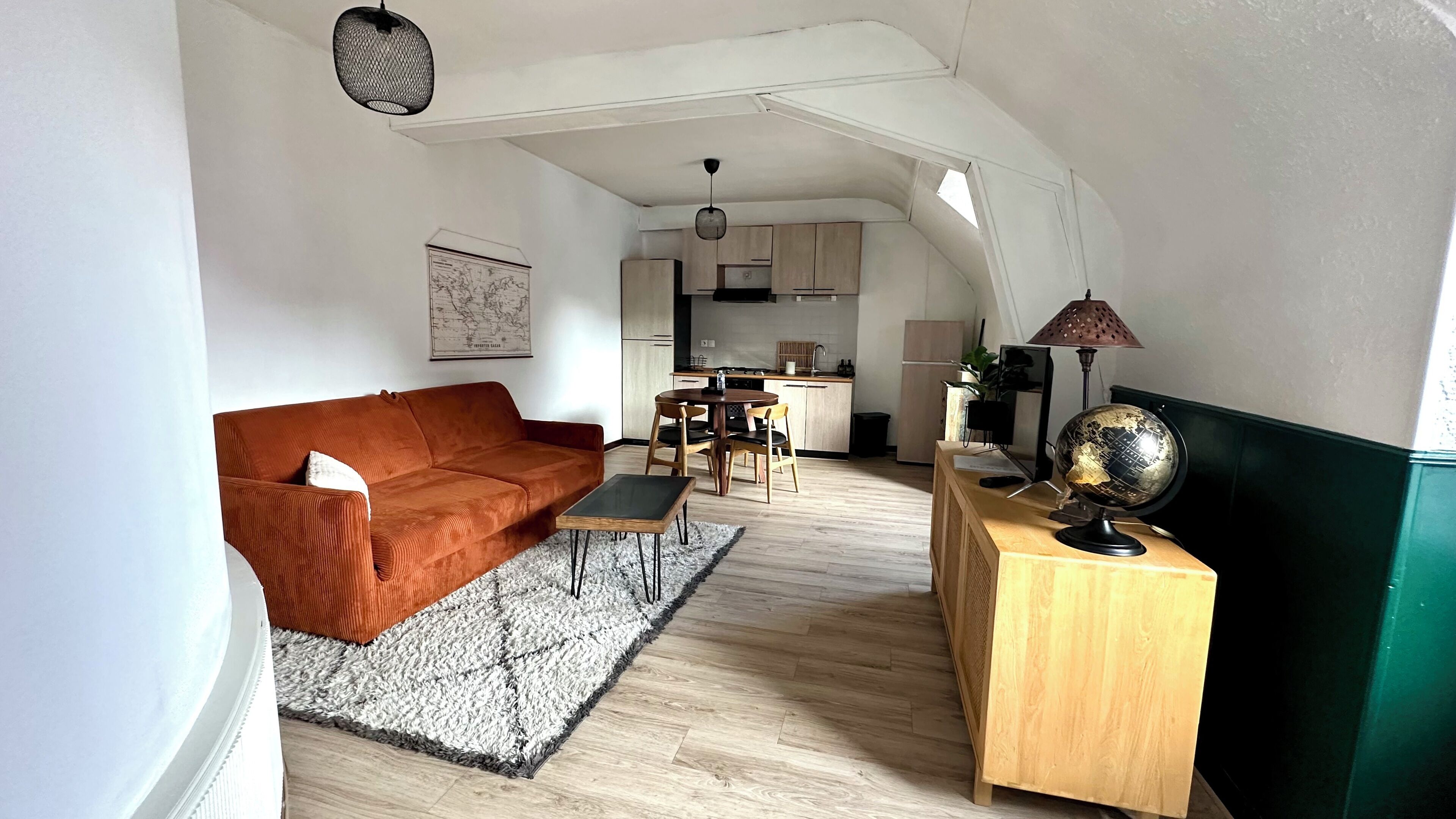 A compact living space with a sofa, a dining table with chairs, a small kitchen area, and a globe on a wooden side table.