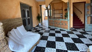 Un hall d’entrée avec un sol à carreaux, un canapé en osier et un escalier.