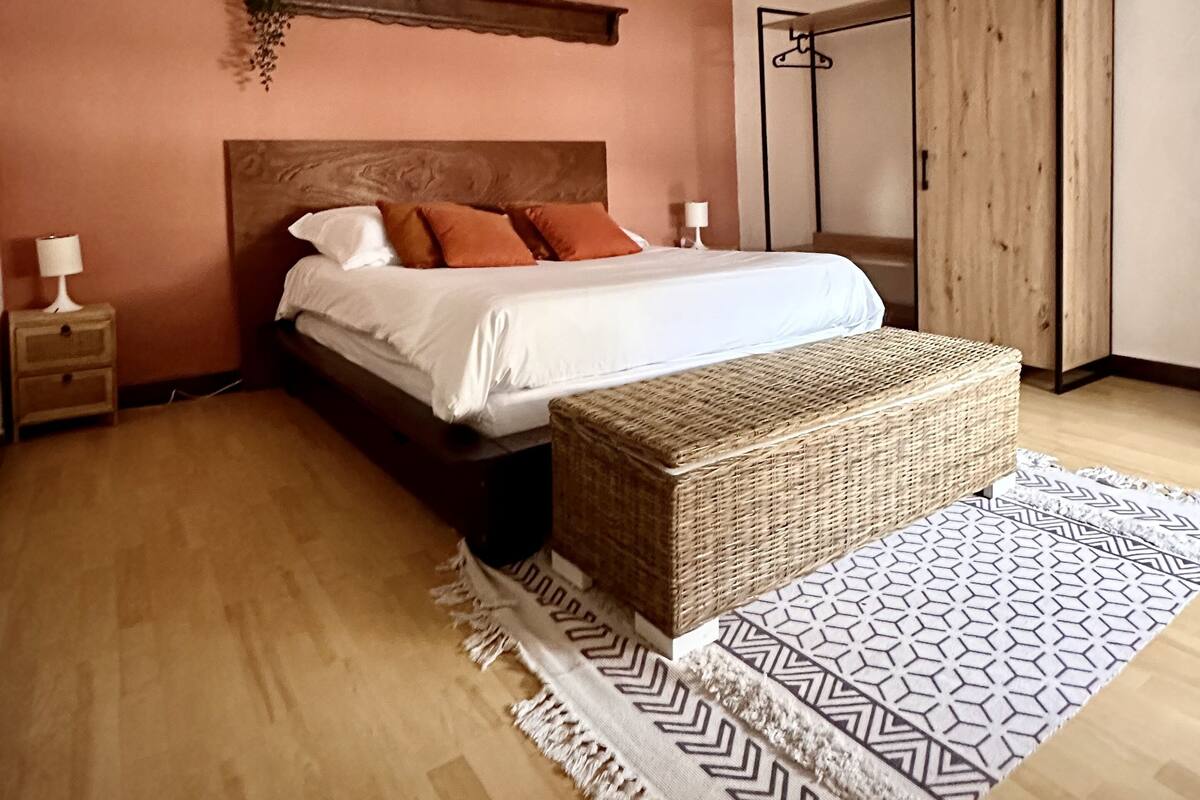 Ein Schlafzimmer mit Bett, Nachttischen, einer Hängelampe, einem Holzschrank und einem gemusterten Teppich.