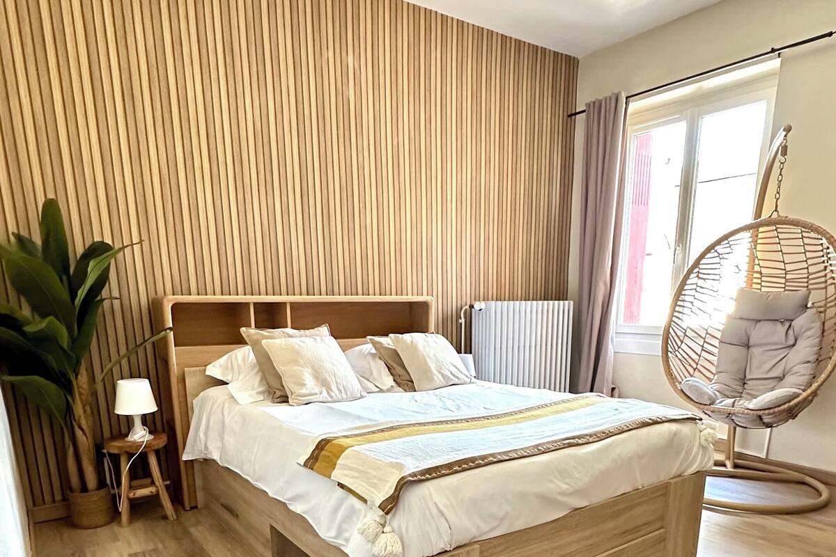 Ein Schlafzimmer mit einem hölzernen Bett, einem Hängekorbstuhl und einer Topfpflanze.