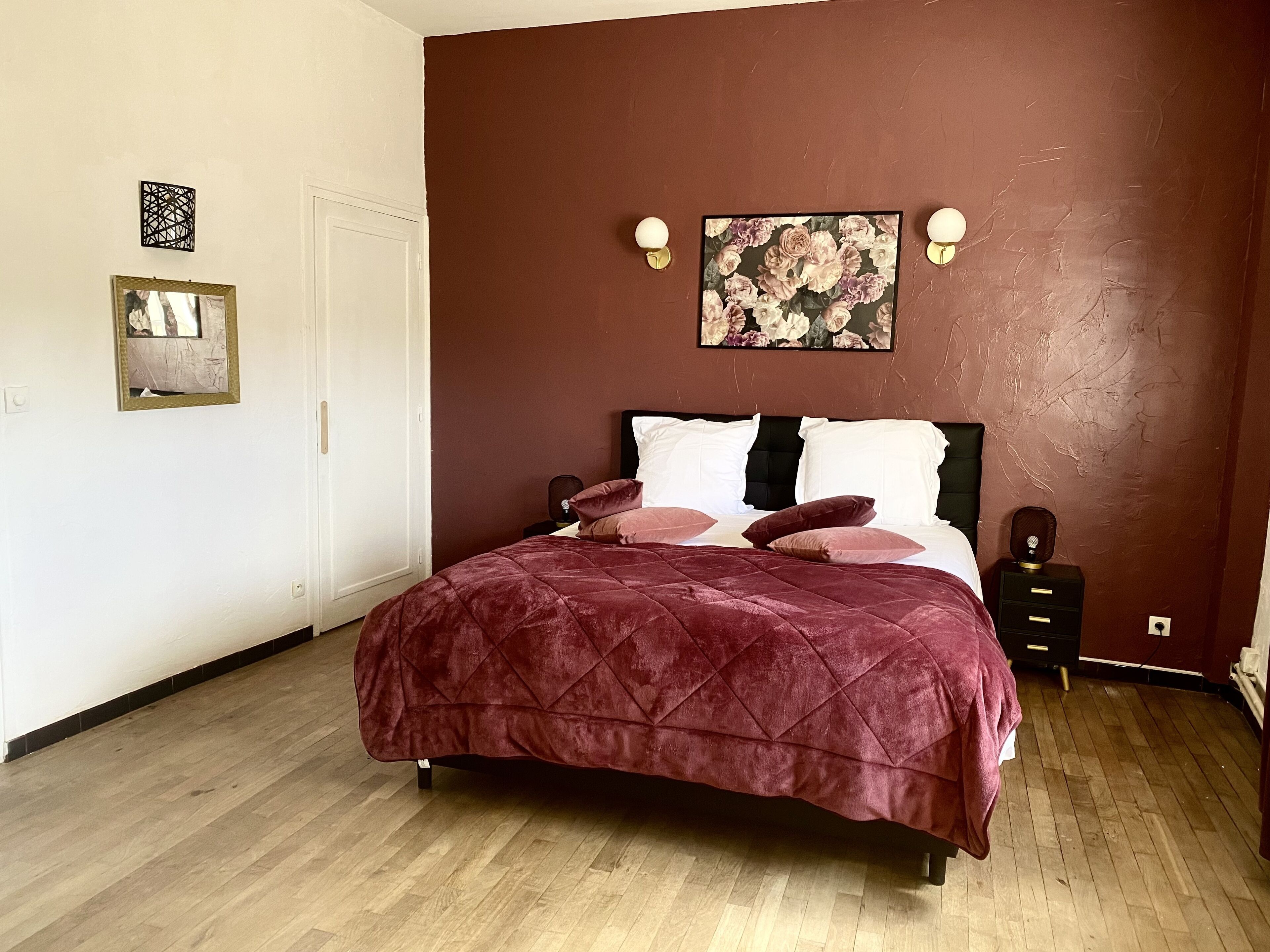 A bedroom with a bed, a nightstand, a wall-mounted light, and a framed picture.