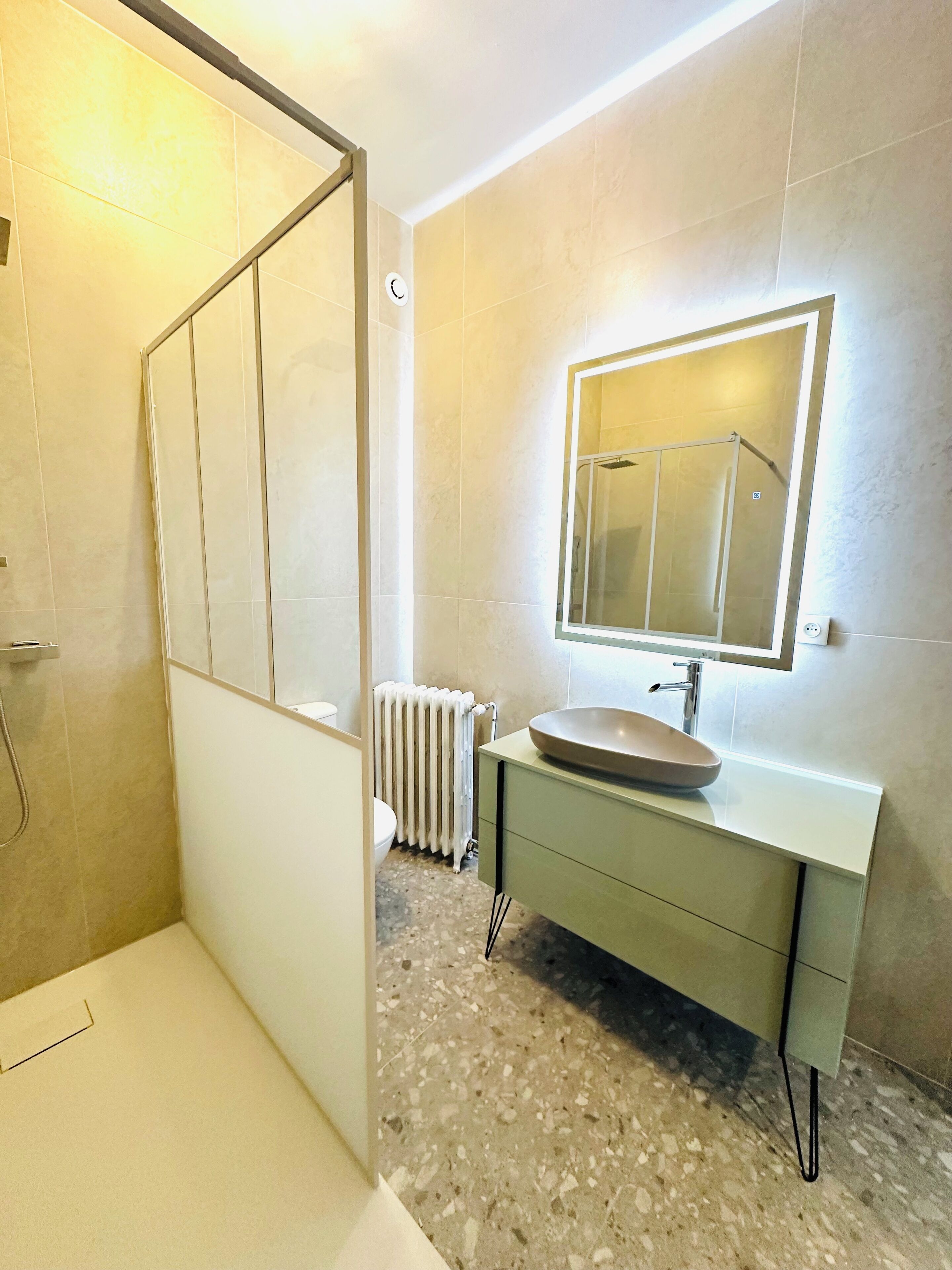 Une salle de bain moderne avec une baignoire, un lavabo surmonté d’un grand miroir et un radiateur au sol.