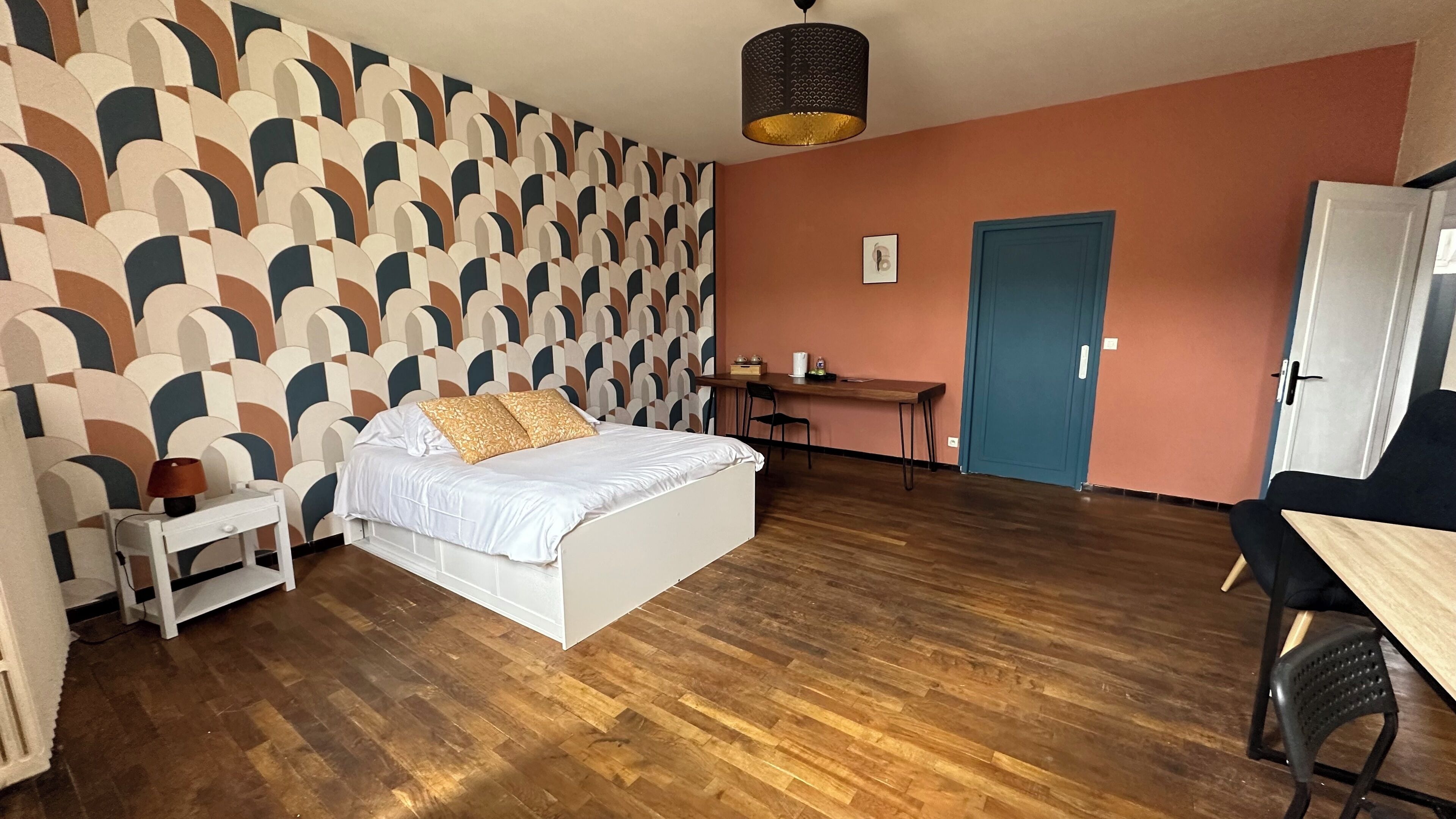 Un dormitorio con pared estampada, una cama, un escritorio y una silla.