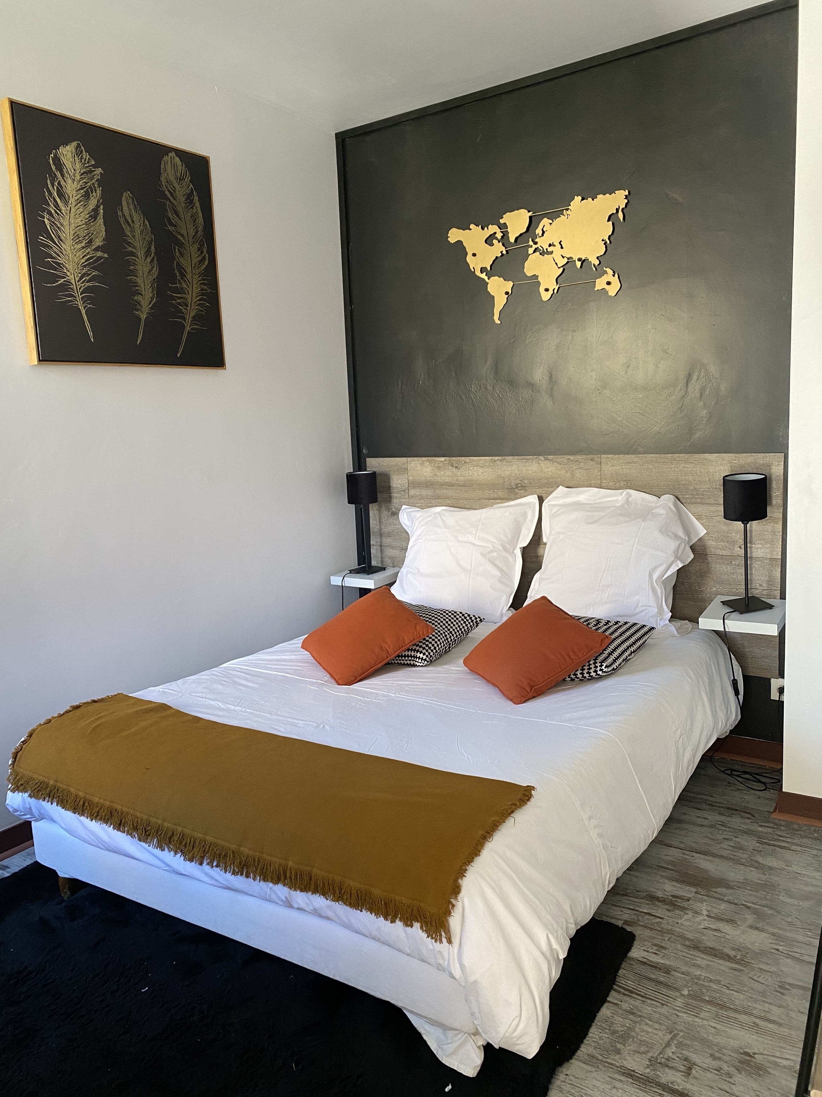 A neatly made bed with white and brown bedding, two white pillows, and two orange pillows. A world map is displayed on the wall above the bed.