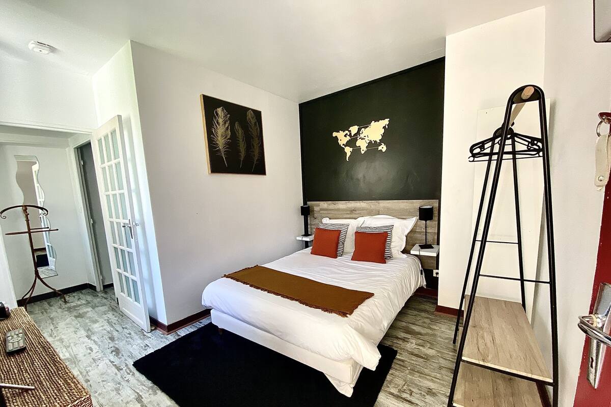 Ein Schlafzimmer mit einem großen Bett, einer Weltkarte an der Wand, einer schwarz-weiß Lampenleuchte und einer Holzleiter.