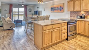 A modern kitchen with wooden cabinets, a central island, and a dining area with a view to the outside. - 2 BR/2.5 BA beautiful, spacious waterfront Carolina Beach condo (Carolina Beach)
