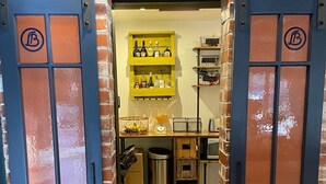Un ingresso che dà su una stanza con un muro in mattoni, uno scaffale con bottiglie e un cestino.
