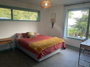 A bedroom with a bed, a bedside table, a chair, a window, and a wall-mounted light fixture.