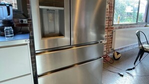 Un frigorifero in acciaio inossidabile in una cucina con parete in mattoni, una finestra e un termosifone.