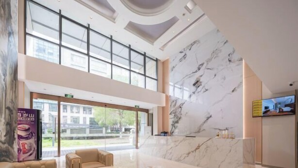 A modern hotel lobby with a marble reception desk, leather seating, large windows, and a TV screen. - City Garden Hotel (Suzhou Kunshan Huaqiao Lvdi Avenue) (Kunshan)