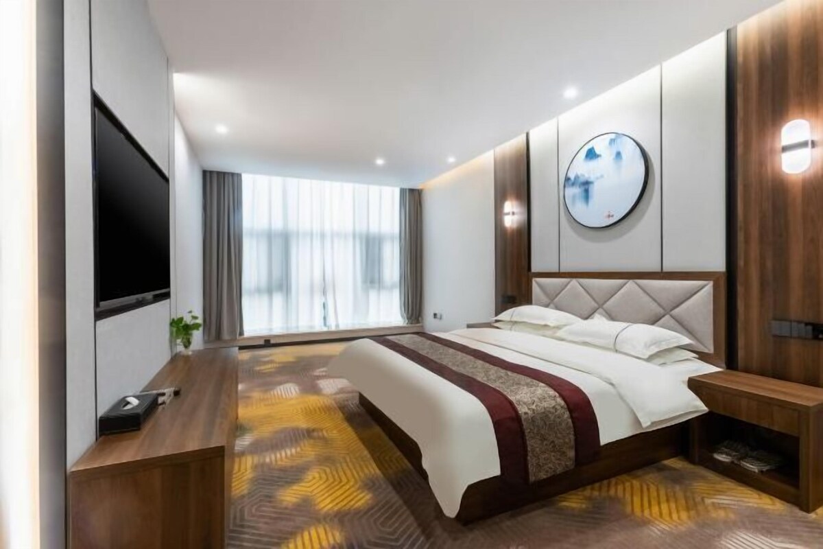Une chambre d’hôtel moderne dotée d’un grand lit, d’un téléviseur à écran plat, d’un bureau en bois et d’une grande fenêtre avec des rideaux.