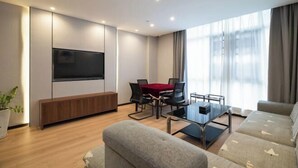 A modern living room with a flat-screen TV, a wooden bench, a glass coffee table, and a sofa. - City Garden Hotel (Suzhou Kunshan Huaqiao Lvdi Avenue) (Kunshan)