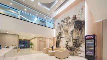 A spacious lobby with a high ceiling, a large mural, seating area, and a vending machine.