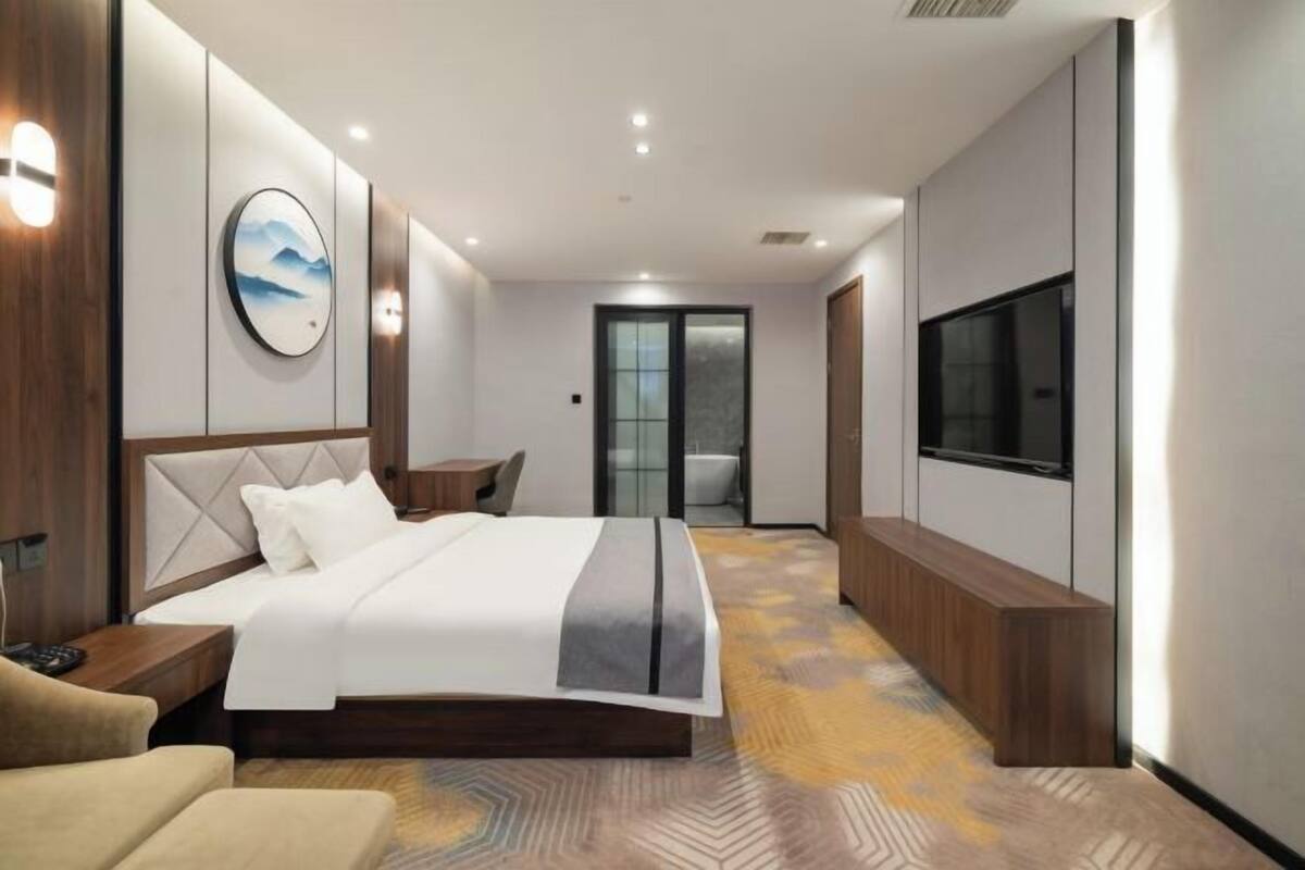 Habitación de hotel moderna con cama, mesita de noche, televisor y vista al pasillo.