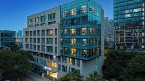 A modern building with a glass facade, multiple floors, and a visible entrance with a sign. - City Garden Hotel (Suzhou Kunshan Huaqiao Lvdi Avenue) (Kunshan)