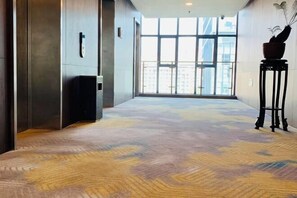 Un couloir moderne avec un tapis à motifs, une grande fenêtre et une plante en pot posée sur une table d’appoint.
