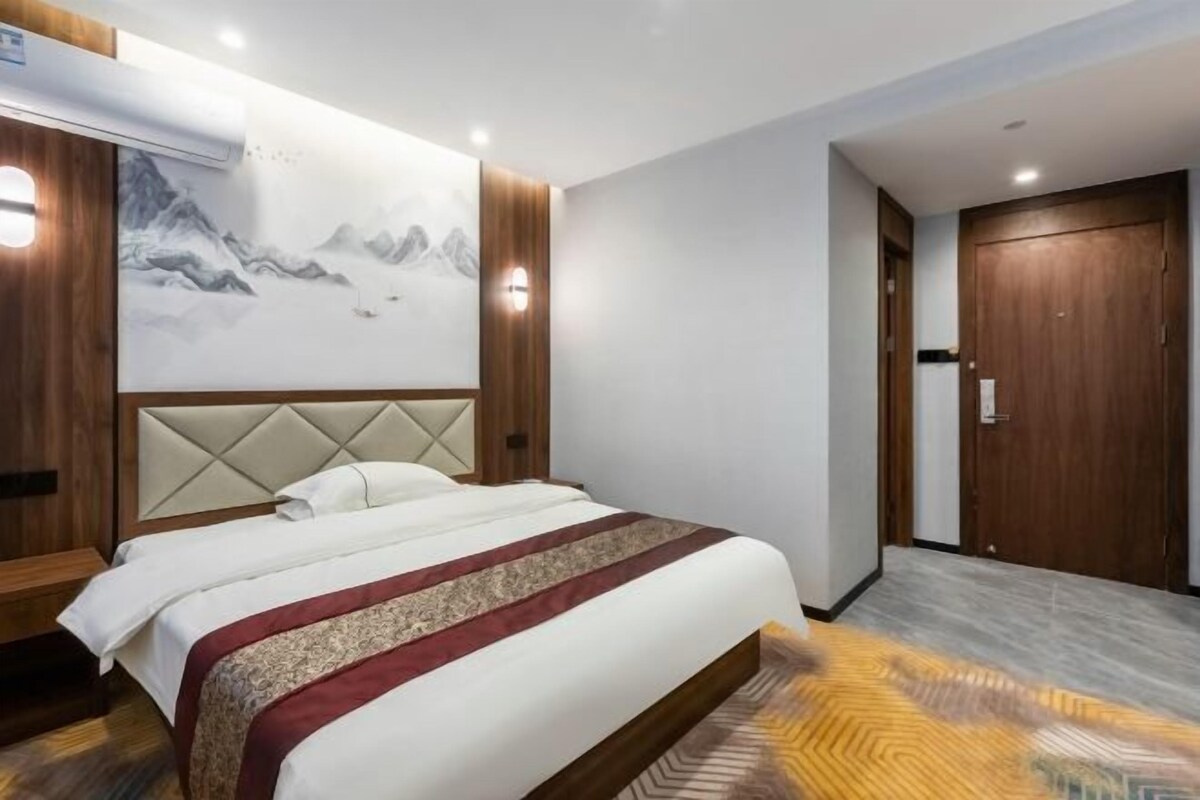 Une chambre d’hôtel avec un grand lit, une tête de lit en bois, un climatiseur fixé au mur et une porte dotée d’une poignée.
