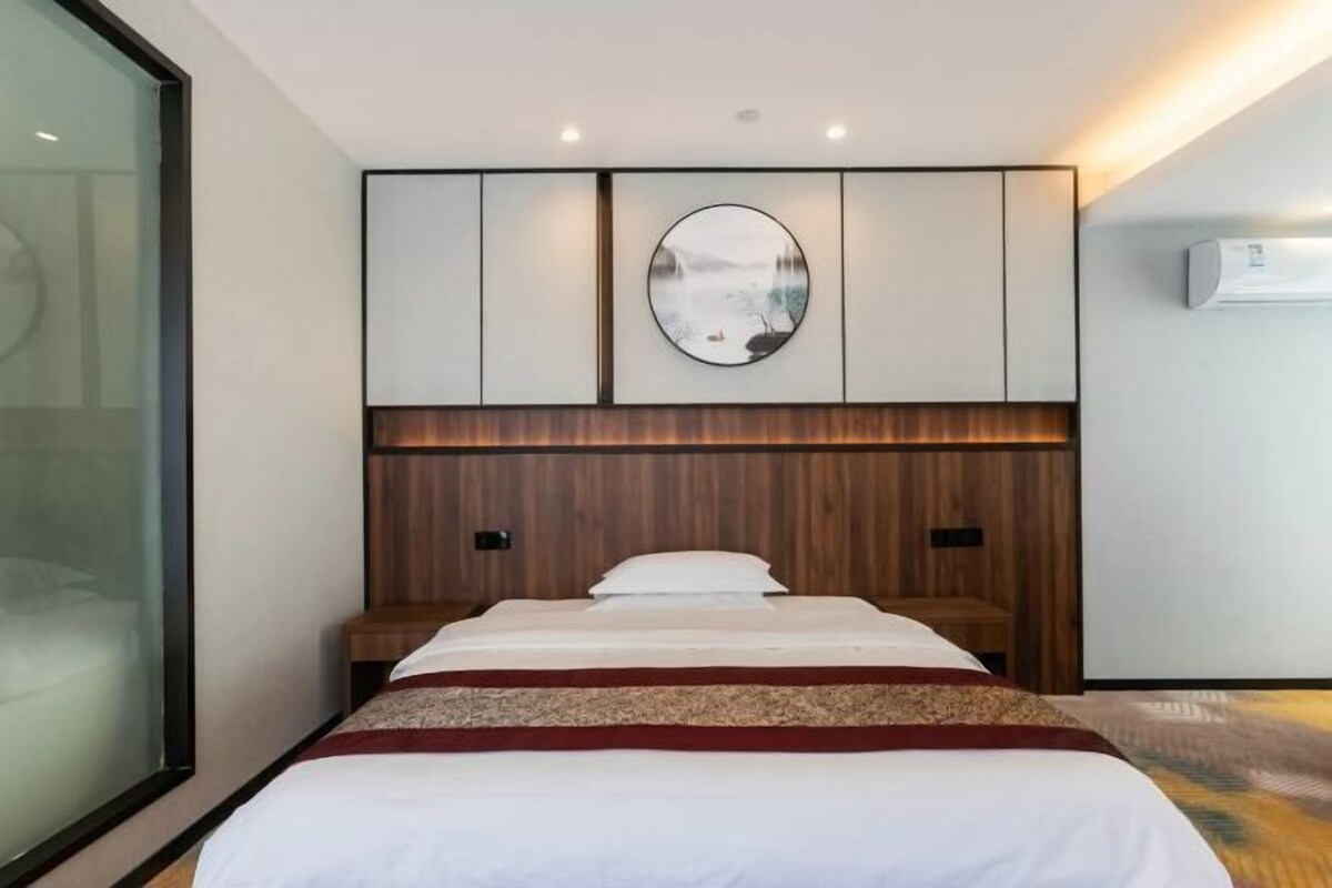 Une chambre d’hôtel moderne dotée d’un grand lit, d’une tête de lit en bois, d’un grand miroir rond fixé au mur et d’un système de climatisation intégré.