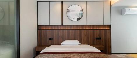 A modern hotel room with a large bed, a wooden headboard, a wall-mounted circular mirror, and a built-in air conditioning unit.