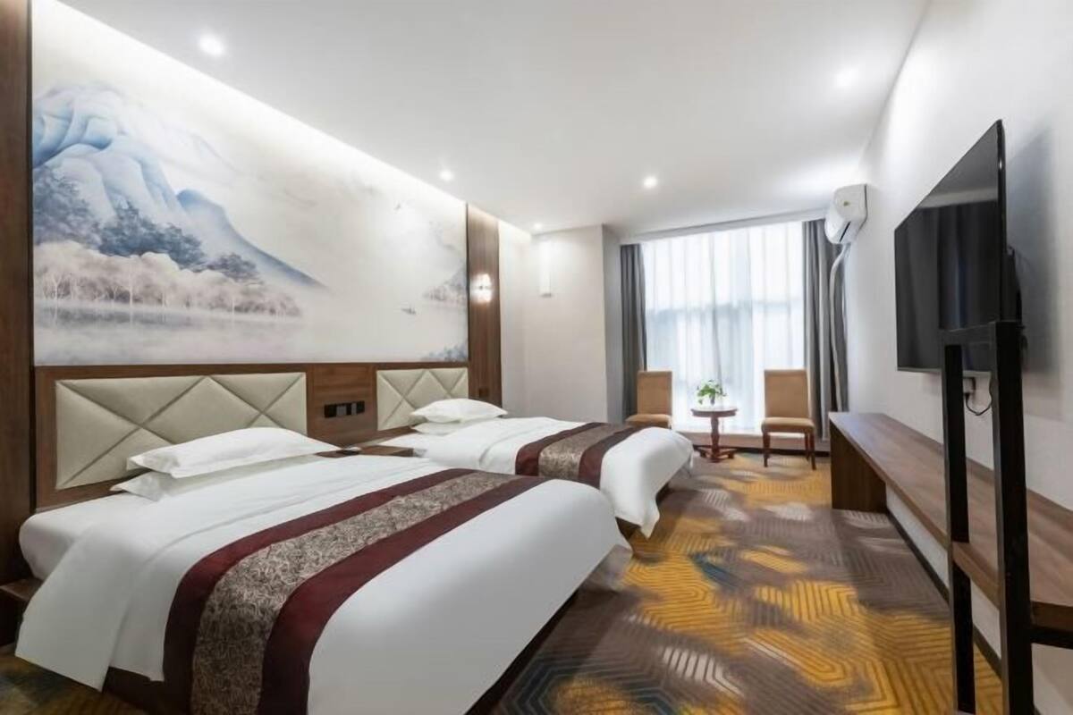 Habitación de hotel con dos camas, un cuadro grande en la pared, un televisor y una ventana con cortinas.