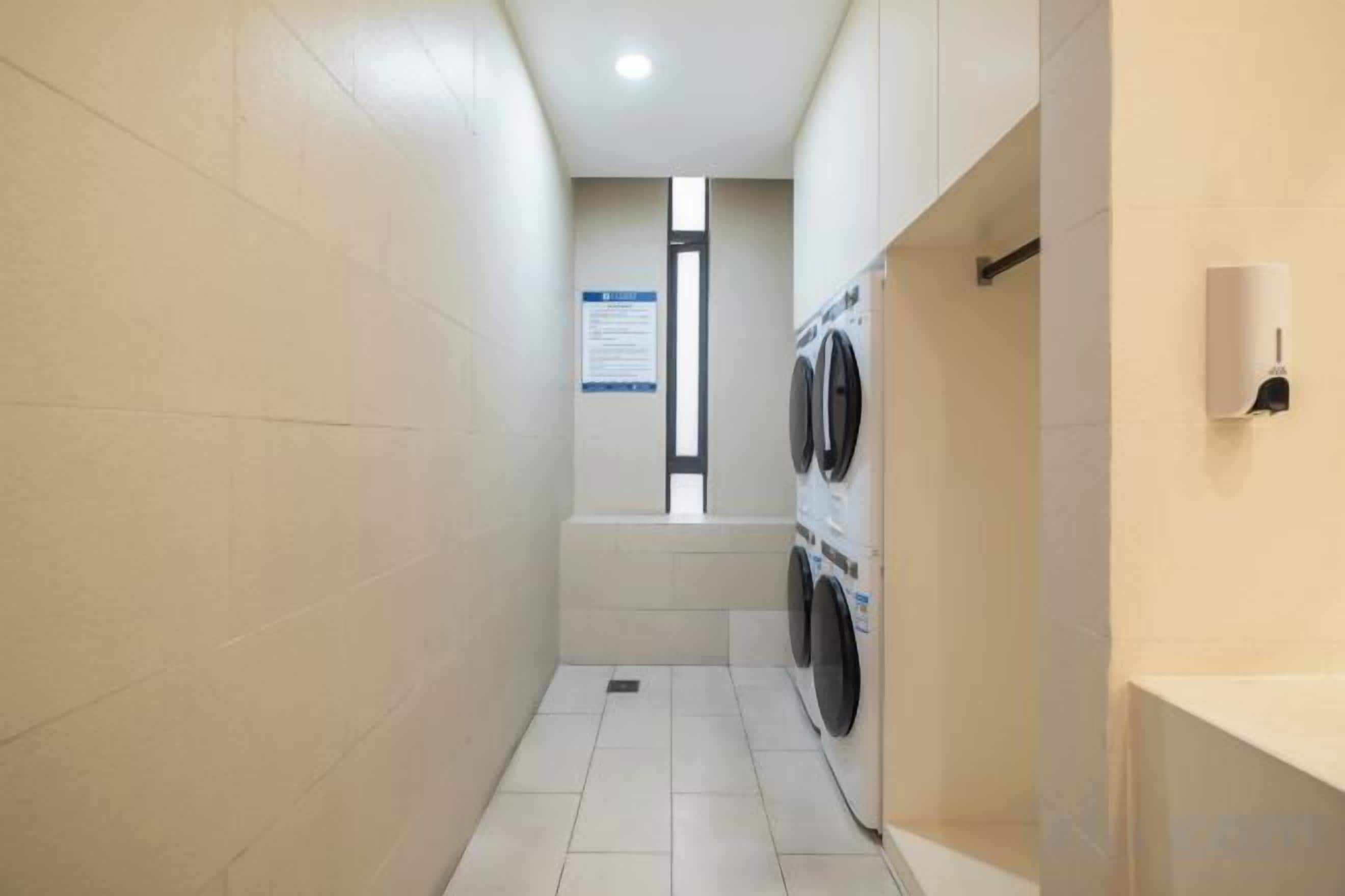 Une buanderie équipée d’un lave-linge et d’un sèche-linge, dotée d’un sol carrelé et d’un distributeur de savon fixé au mur.