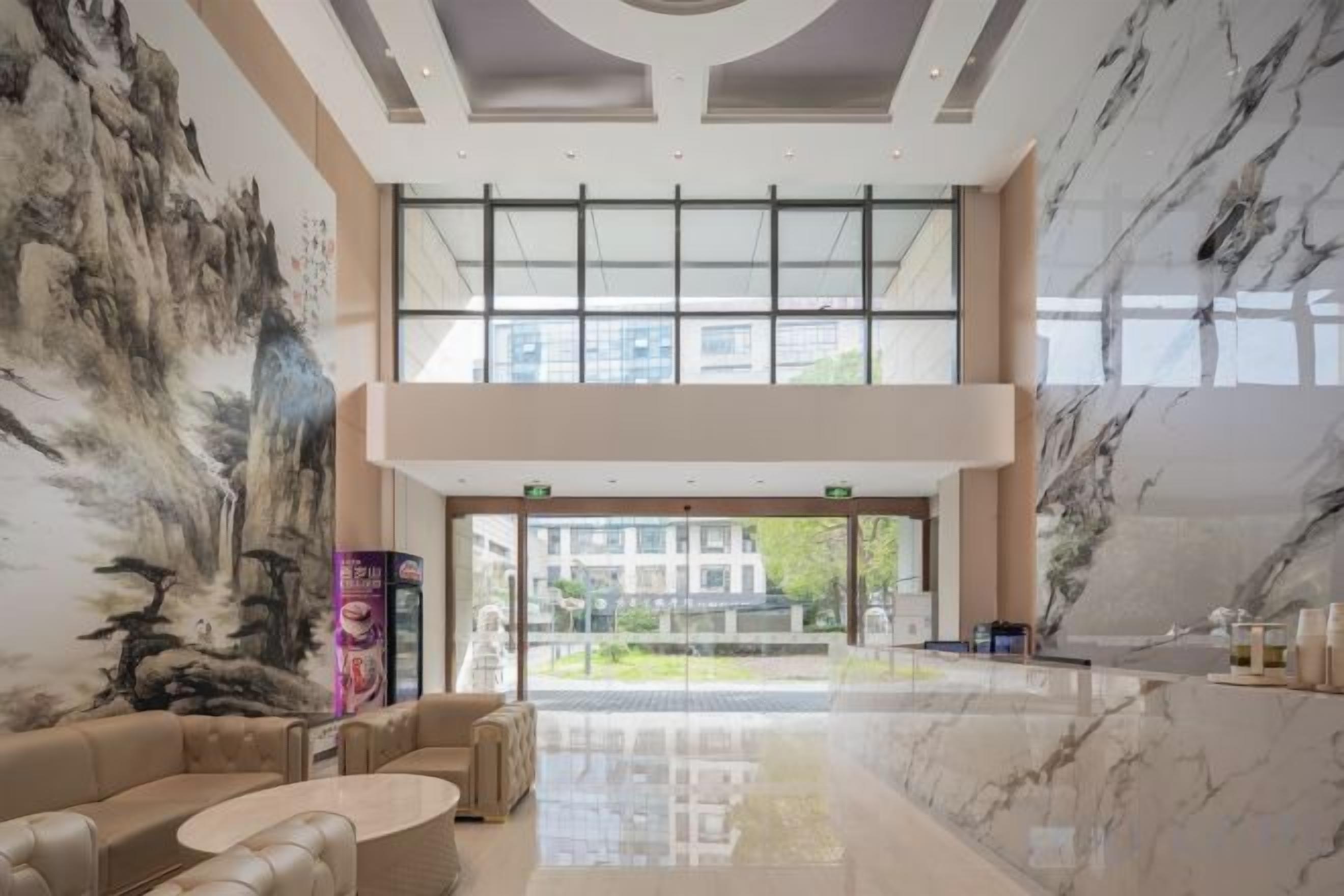 A spacious lobby with a high ceiling, a large painting on the wall, and a view of the outside through large windows.
