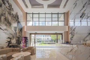 A spacious lobby with a high ceiling, a large painting on the wall, and a view of the outside through large windows. - City Garden Hotel (Suzhou Kunshan Huaqiao Lvdi Avenue) (Kunshan)