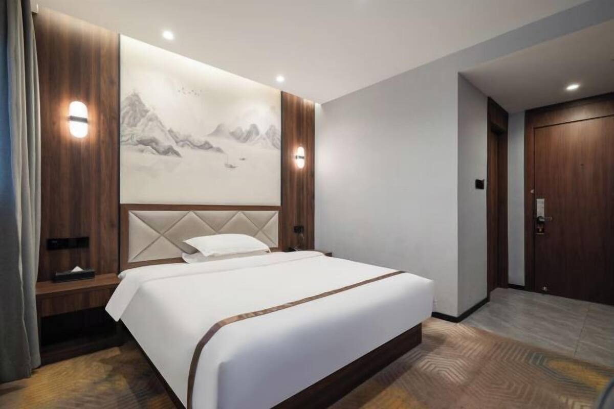 Habitación de hotel con una cama grande, cabecero de madera y una obra de arte en la pared que representa montañas.