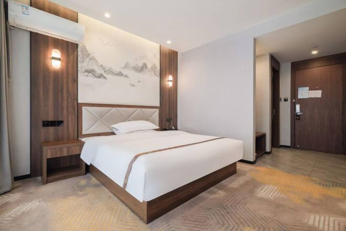 Una habitación de hotel moderna con una cama grande, cabecera de madera y aire acondicionado de pared.