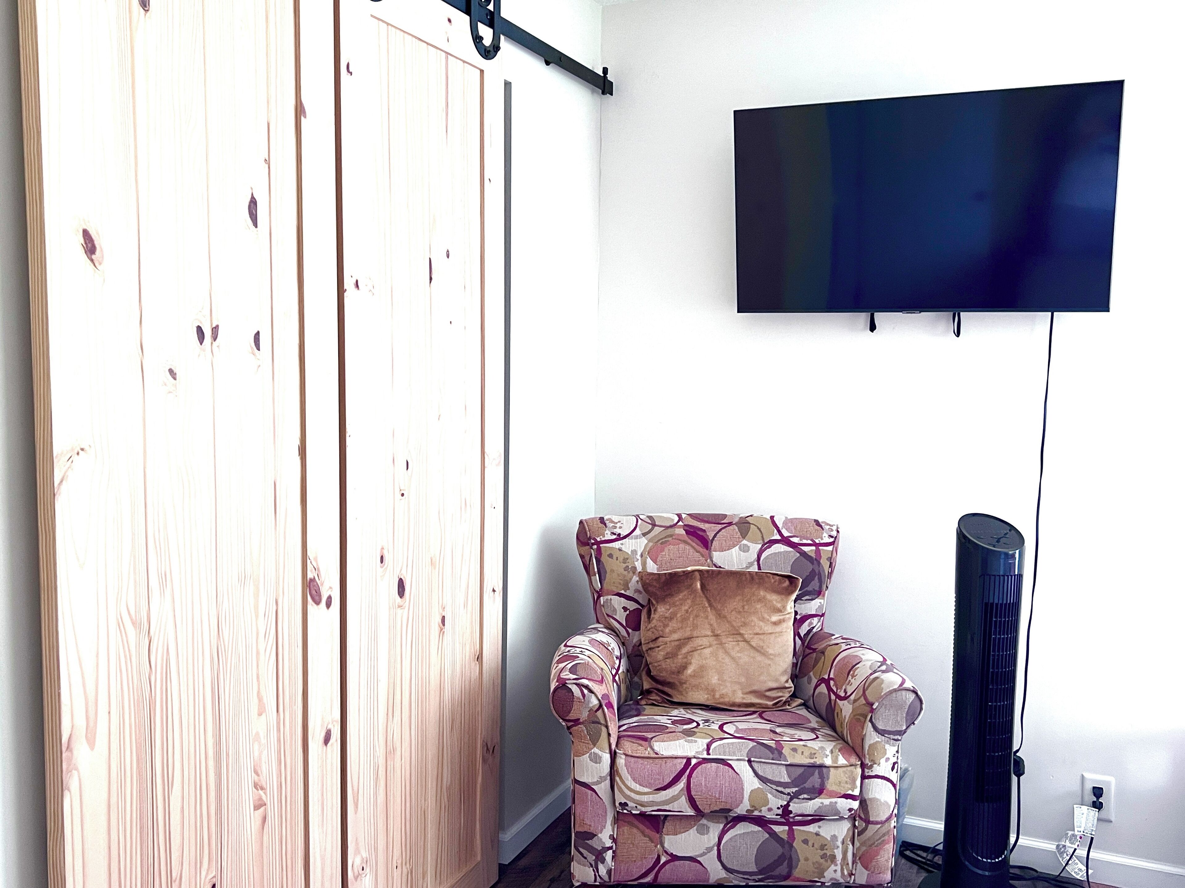Una habitación con un divisor deslizante de madera, un sillón estampado con un cojín y un televisor fijado en la pared.