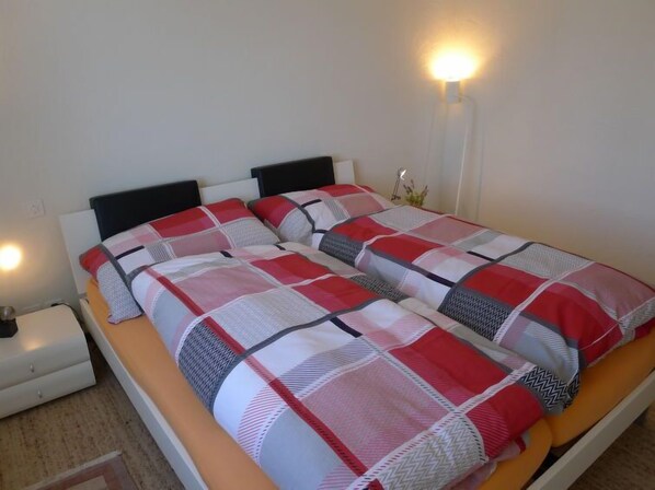 A bed with a checkered bedspread in red, white, and gray.