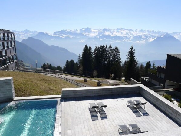A rooftop pool with lounge chairs and a view of snow-capped mountains.