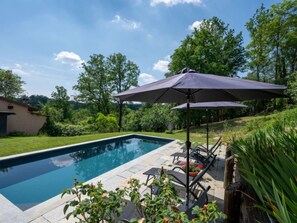 Una piscina rectangular con solárium empinado, rodeada de exuberante vegetación y árboles.