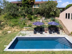 Une piscine rectangulaire bordée de pierres, deux chaises longues et deux parasols.